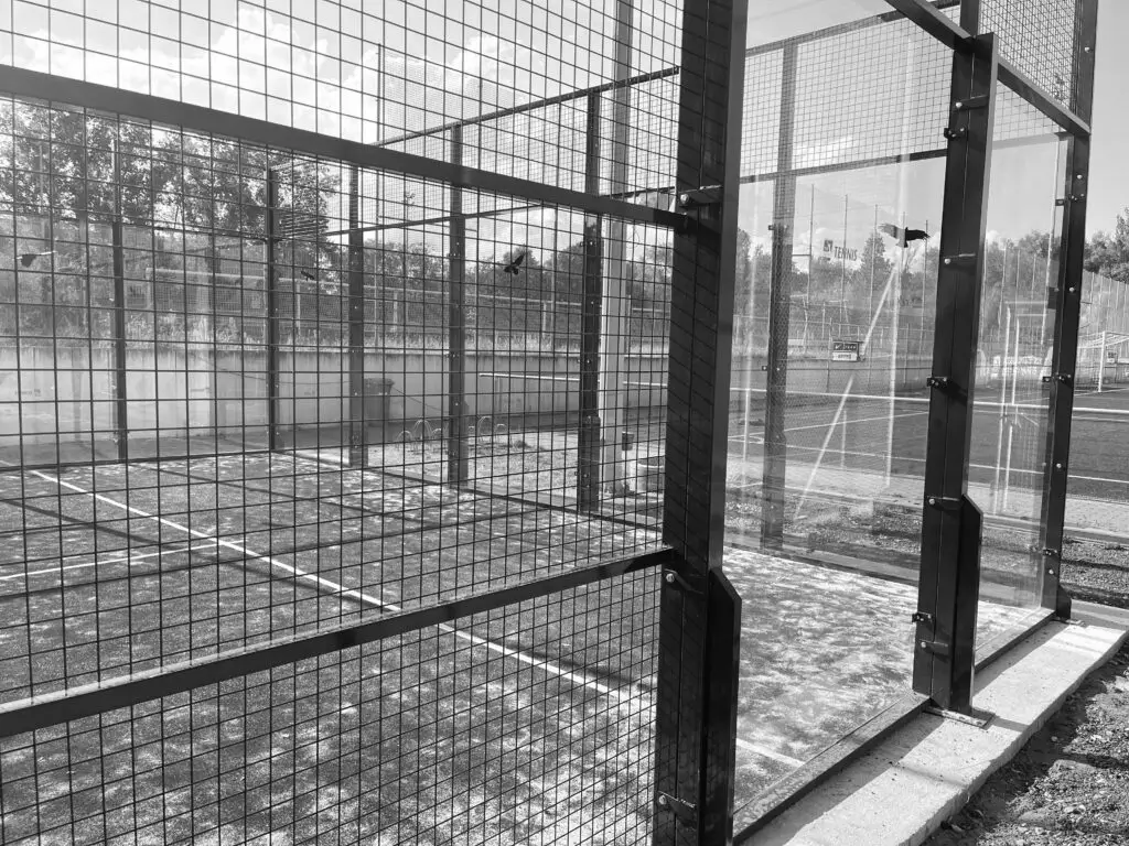 View of a padel court fence, highlighting the glass panels and wire mesh surrounding the court.