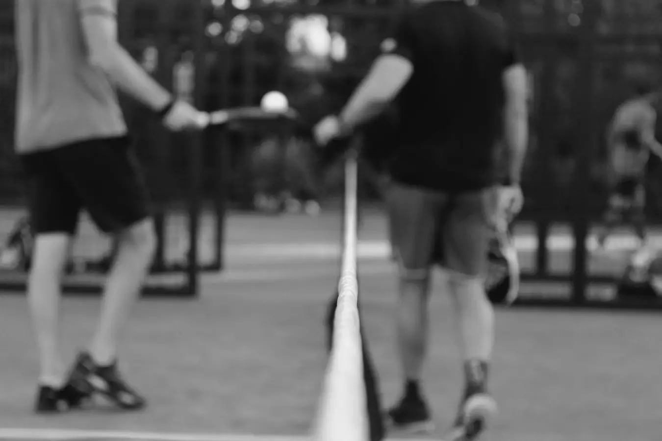 A black and white image showing two padel players standing near the net, holding their rackets, with the focus on the net cord in the foreground.