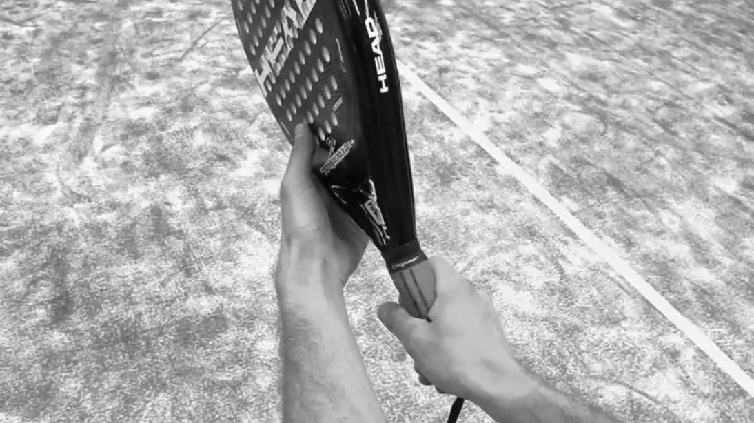 Close-up of a player adjusting their padel racket grip on the court.