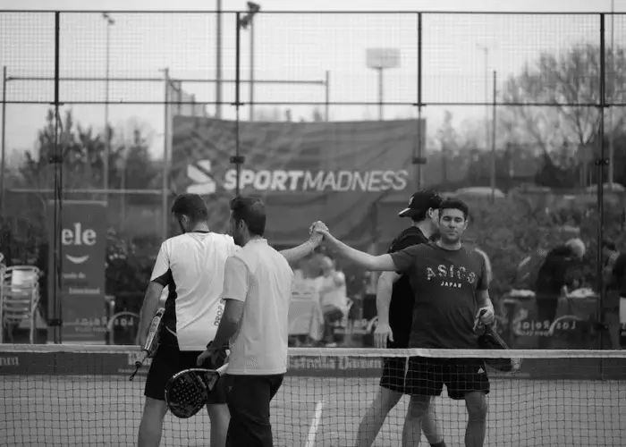 Padel players shaking hands across the net after a doubles match, with a 'Sportmadness' banner in the background.