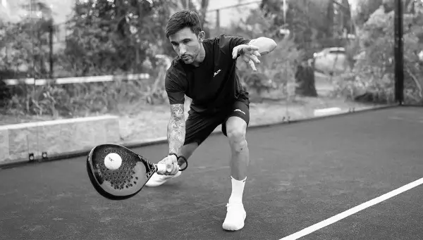 A padel player prepares to execute a low, controlled lob shot while focusing on ball placement and timing.