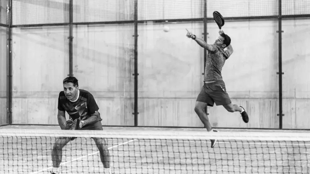 Two men playing padel, one jumping for an overhead smash while the other is positioned at the net, ready for the next move.