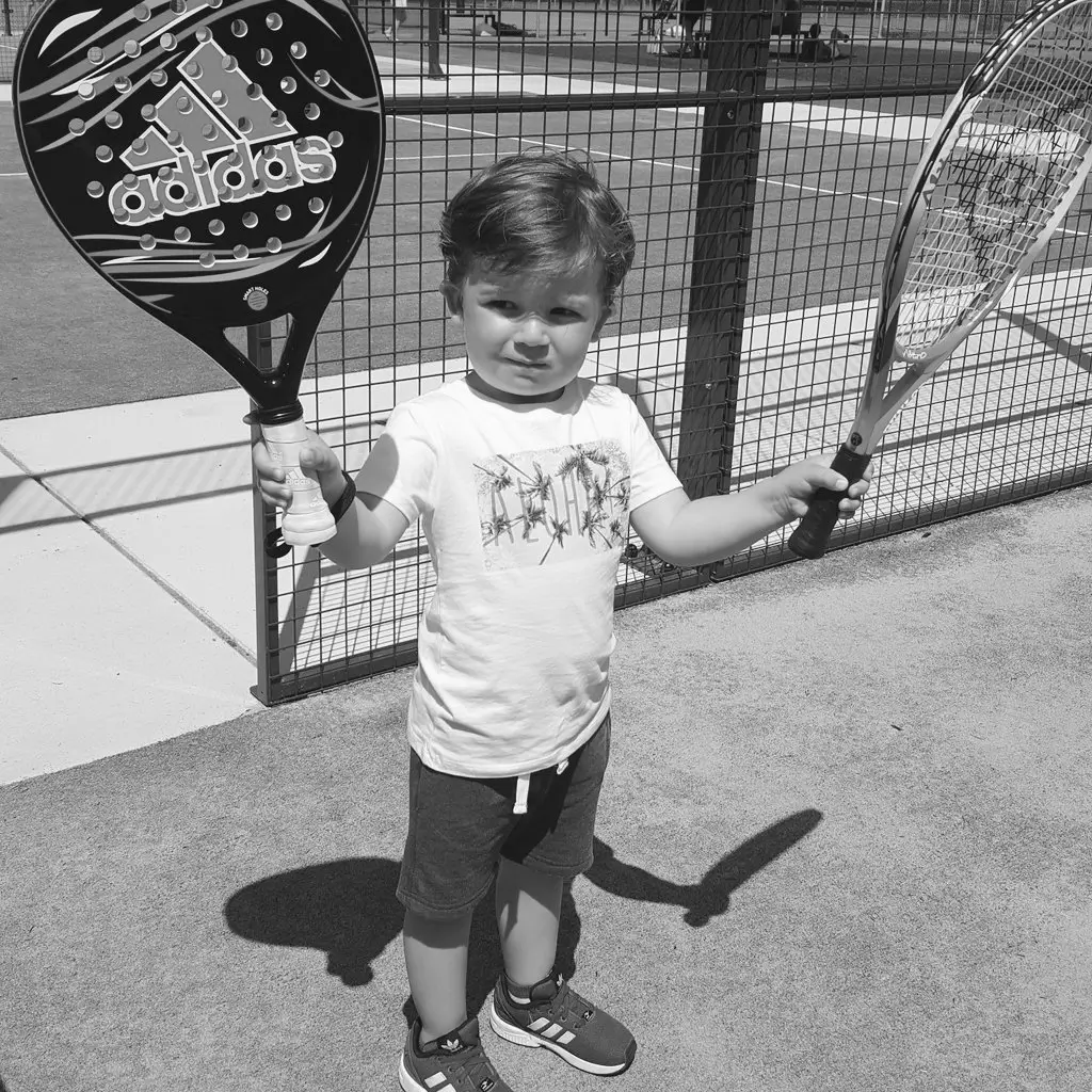 Young kid holding padel and tennis rackets on a court, confidently ready to play.