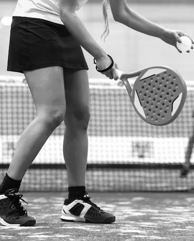 Female padel player preparing to serve, holding ball and paddle in ready position on the court.