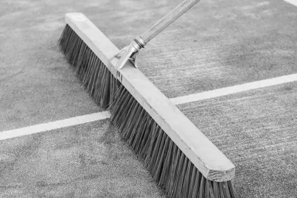 Large broom sweeping an artificial turf padel court to maintain even sand distribution and cleanliness.