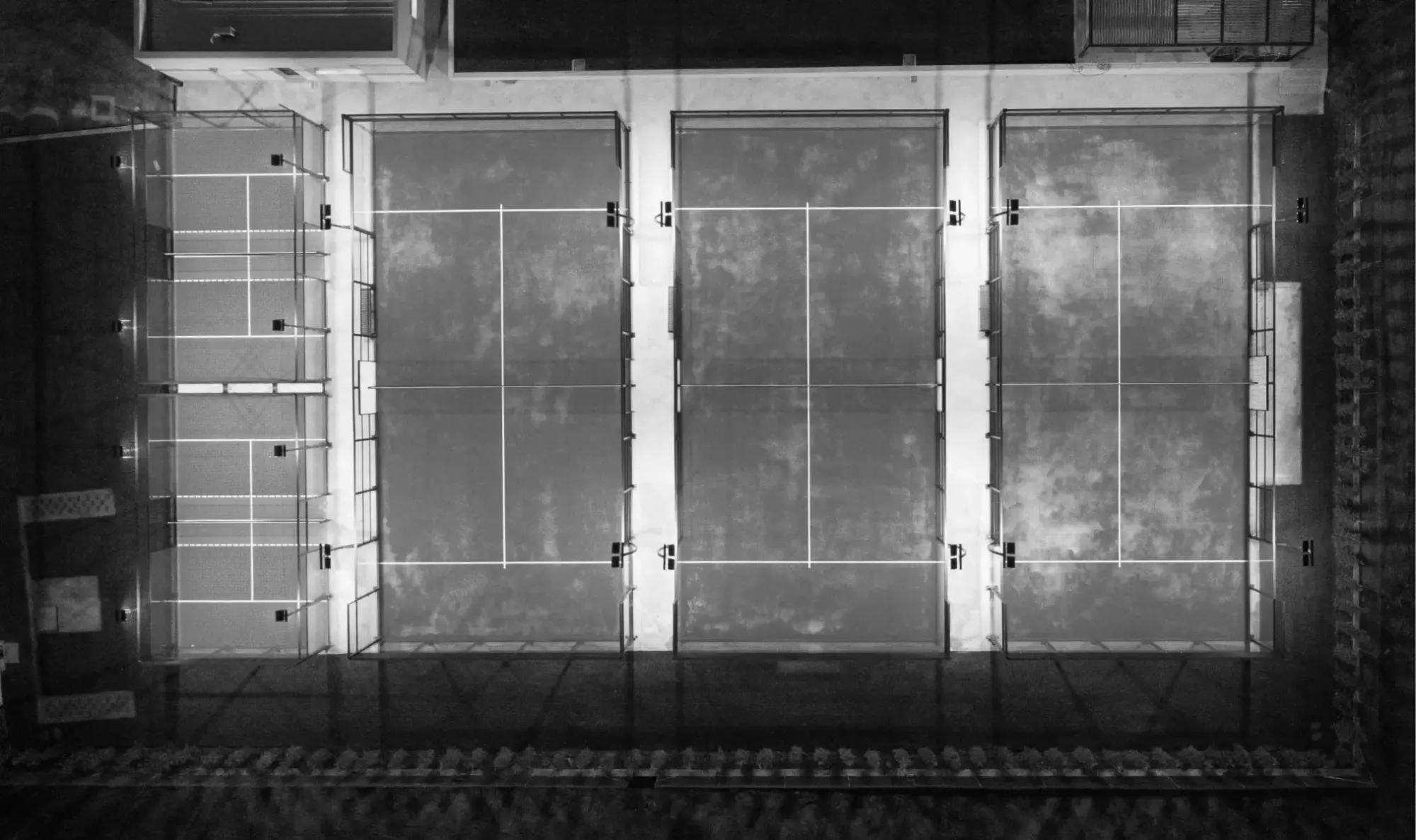 Top-down view of illuminated padel courts at night, highlighting the layout and enclosed design of the playing area.