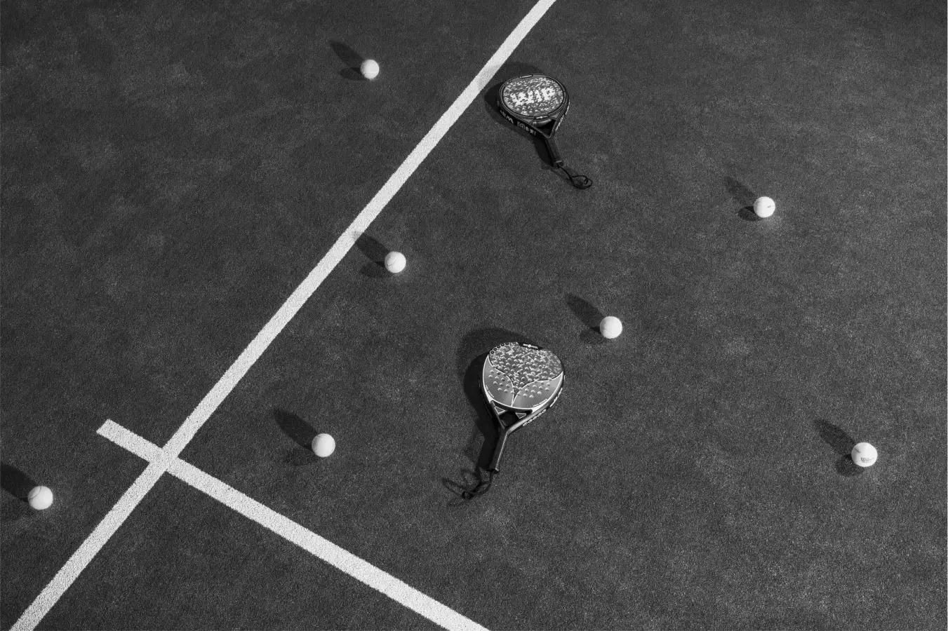 Two padel rackets and several balls scattered across a court, highlighting the sport's essentials and simplicity.