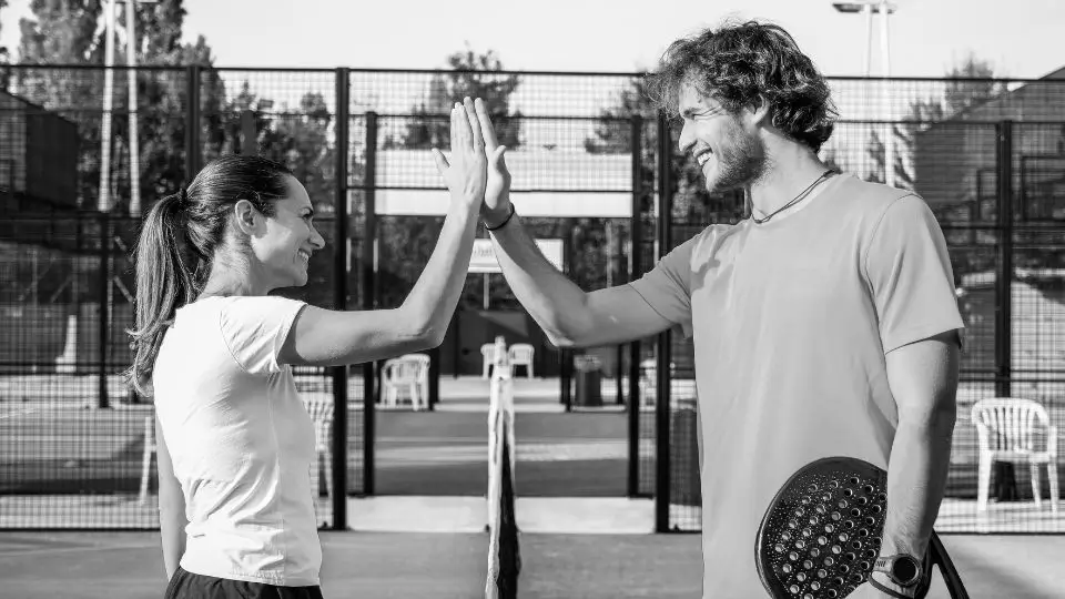 Two padel players sharing a high-five on the court, celebrating teamwork and a positive game spirit.