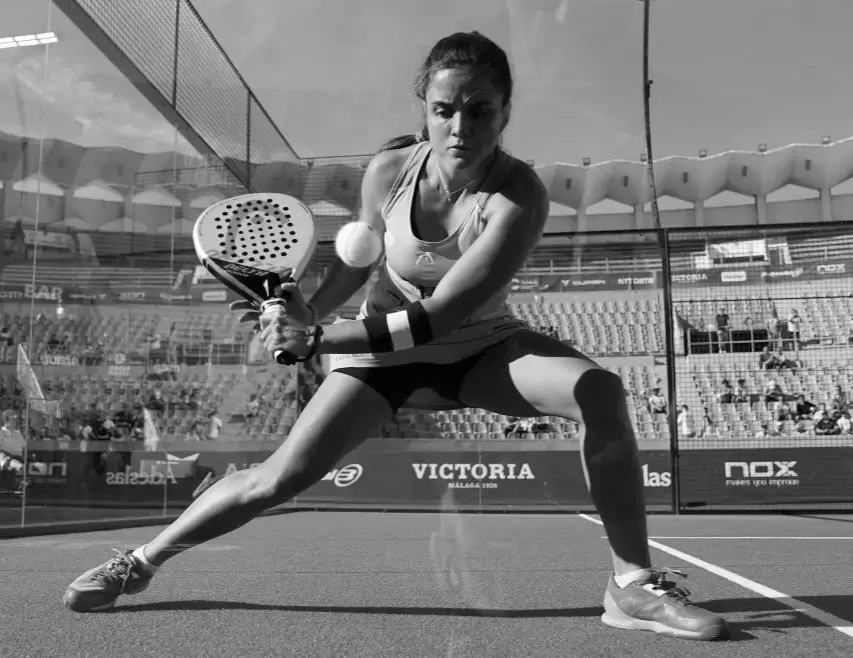 Padel player Paula Josemaría executing a focused double-handed backhand return during an intense match on the court.